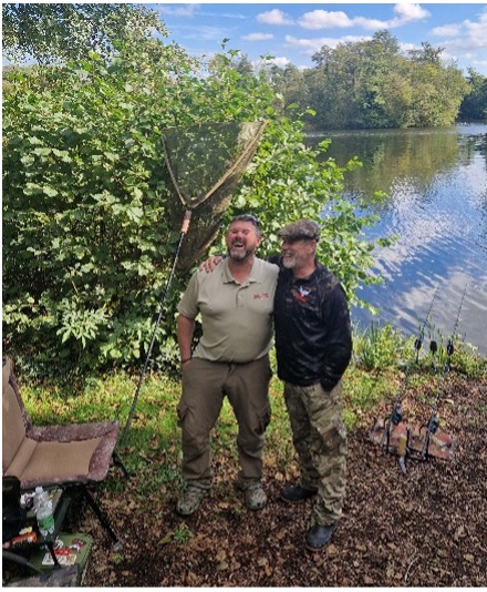 Two men stood by the lake posing for a photograph